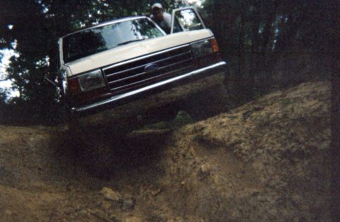 1990 Ford Bronco - A white Ford truck navigates a steep dirt path with its driver's door ajar.