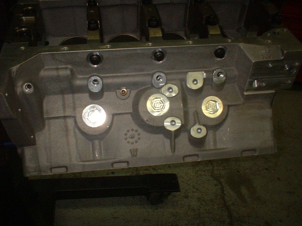 Bare aluminum V8 cylinder head on a bench with machined ports and plugs