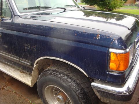 1989 Ford Bronco - Front quarter view of a dark blue 1989 Ford Bronco, showing the fender, wheel, and part of the hood.