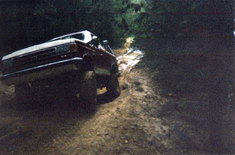 1990 Ford Bronco - 1990 Ford Bronco navigating a challenging muddy trail in a wooded area.