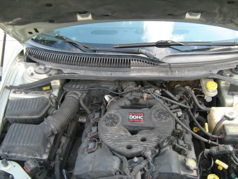 1988 Mercury Grand Marquis - Open engine bay of a light-colored car showing a dusty Chrysler 2.7-liter DOHC 24-valve V6 with its black plastic intake plenum cover, ribb…