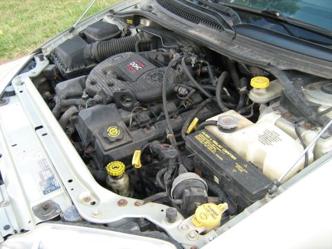 1988 Mercury Grand Marquis - Engine bay of a silver sedan with the hood open, showing a transverse Chrysler 24-valve DOHC V6 with a black plastic intake plenum, black a…