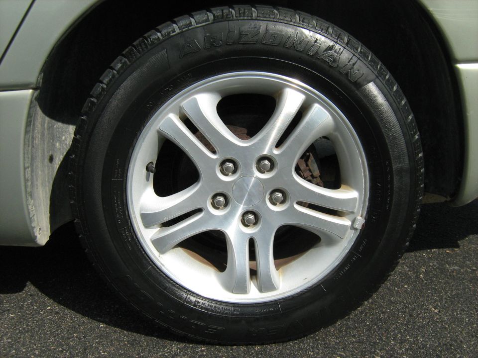 Silver five-spoke wheel with a black tire on a light-colored car