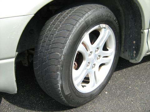 1988 Mercury Grand Marquis - Close-up of the front wheel on a silver car, showing a five-spoke machined-face alloy wheel with center cap and five lug nuts, wrapped in a…