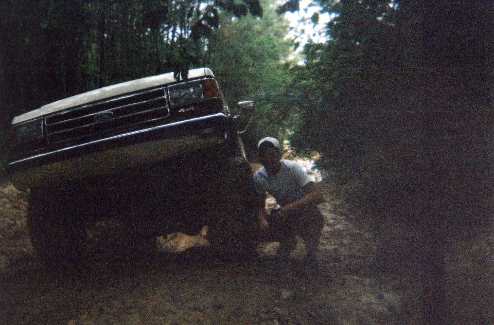 Dark Ford 4x4 SUV tilted on a dirt bank with a person crouching by the front fender