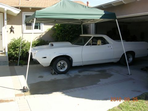1972 Ford Ranchero - A white 1972 Ford Ranchero is parked under a green canopy, showing its distinctive scoop on the hood and a side profile.
