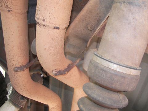 1995 Ford Bronco - Close-up view of rusted exhaust pipes and hangers, likely from a vehicle's undercarriage.