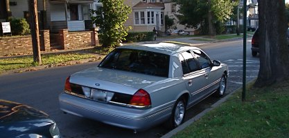 2000 Ford Crown Victoria - A silver 2000 Ford Crown Victoria is parked on the side of a street in a residential area.