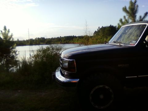 1994 Ford Bronco - A 1994 Ford Bronco is parked near a body of water with trees lining the horizon.