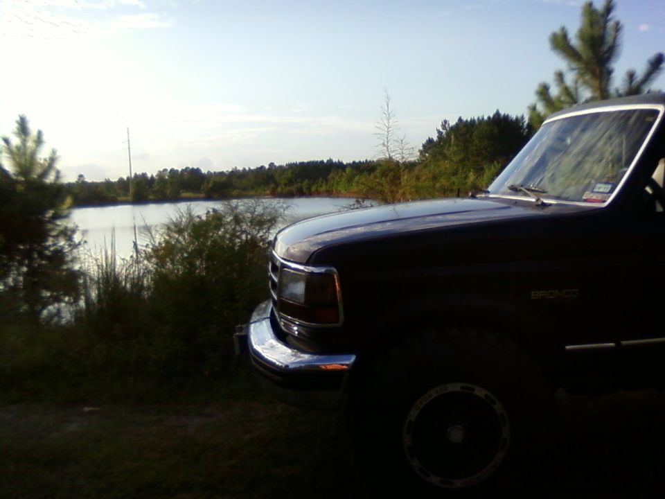 Dark Ford Bronco parked near a lake with trees in the background