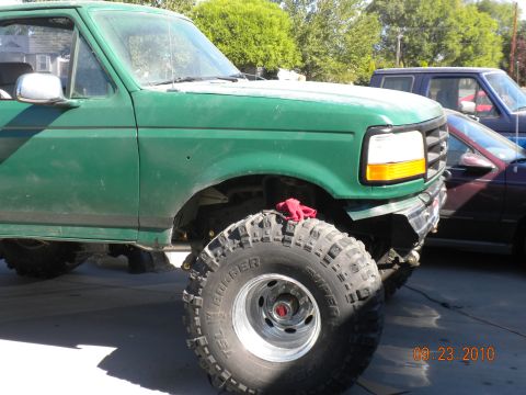 1989 Ford Bronco - 1989 Ford Bronco, lifted with large tires, parked next to another vehicle.