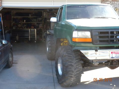 1989 Ford Bronco - A modified green pickup truck with oversized tires is parked in a garage.