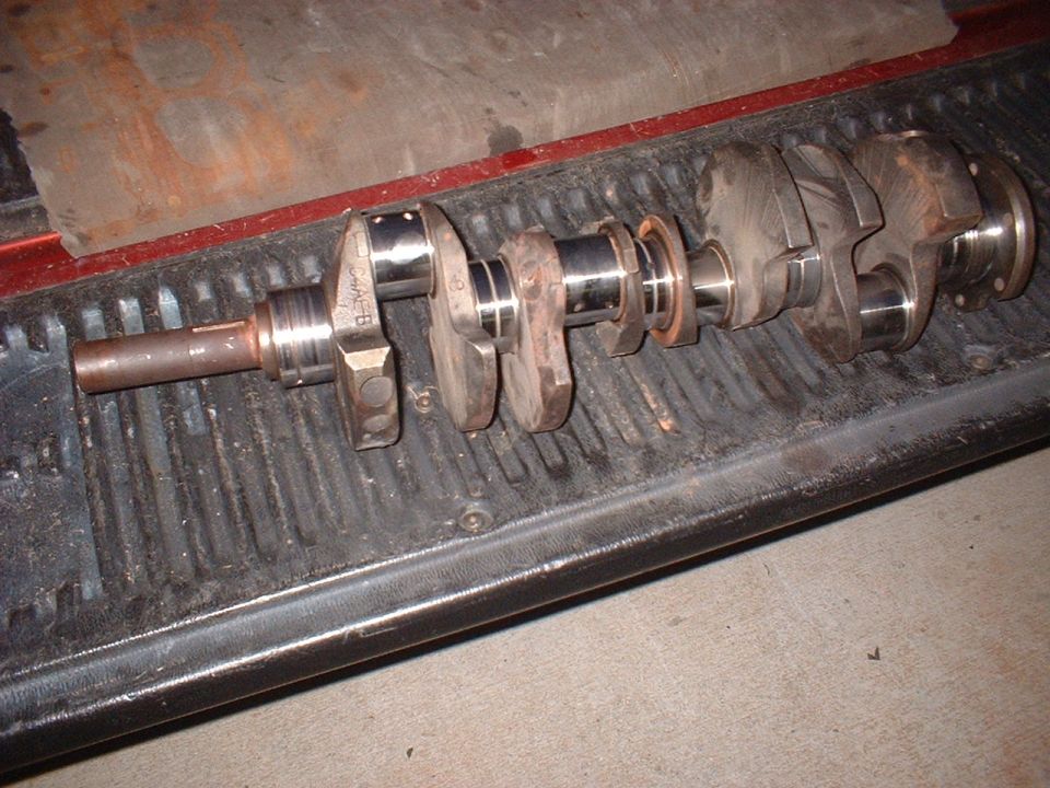 Rusty V8 crankshaft with polished journals lying on a black truck tailgate, casting mark C4AE-B visible