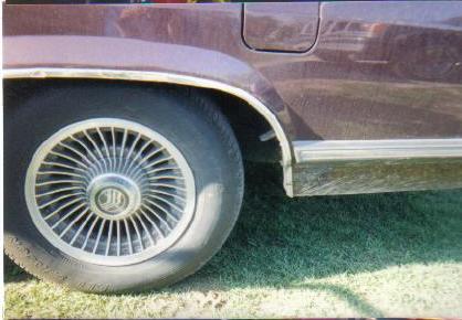 1990 Mercury Grand Marquis - The side profile of a sedan shows its rear wheel and lower body trim. A Mercury logo is visible on the hubcap.