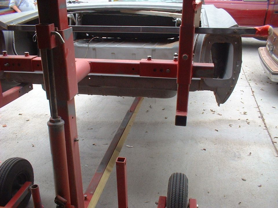 Car frame being worked on by a red lift, with another vehicle visible to the right