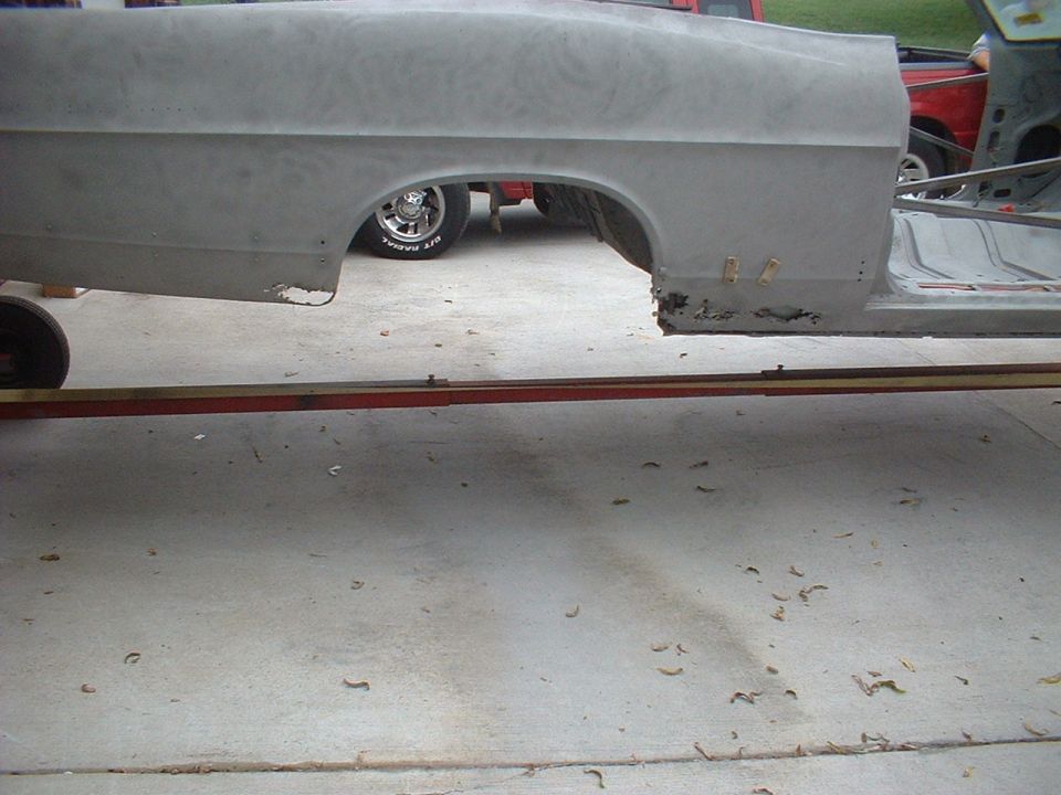 1967 Ford Galaxie quarter panel, bare metal, showing rust damage on lower edge. A red truck is visible behind it