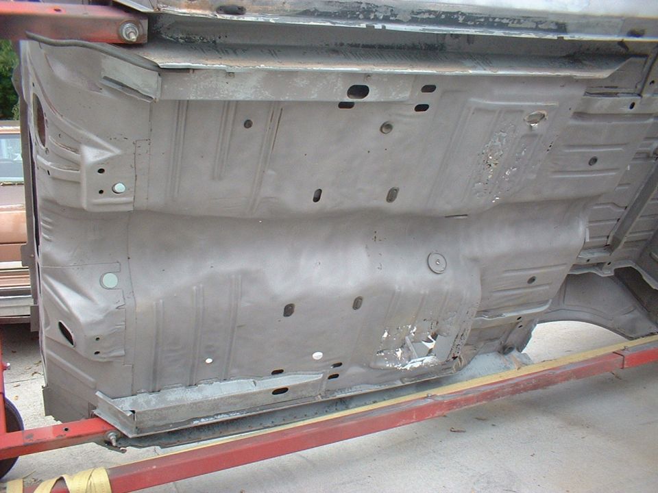 Underside of a car body, showing floor pan and frame rails, supported by a red frame rack