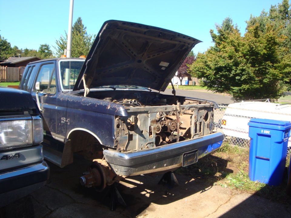 Dark blue Ford truck with front clip removed, on jack stands in driveway