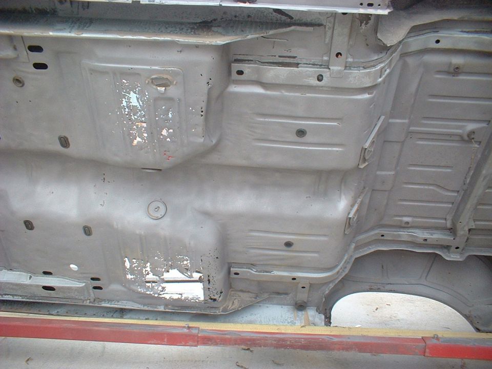 Underside of a car chassis, gray, showing rust and damage, viewed from below