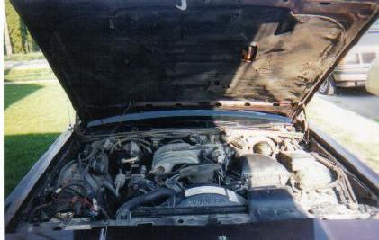 1990 Mercury Grand Marquis - The engine bay of a 1990 Mercury Grand Marquis is visible with the hood raised.