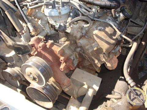 1989 Ford Bronco - Overhead view down into a dirty engine bay with the valve covers and much of the top end stripped, showing a rust-colored cast intake front…