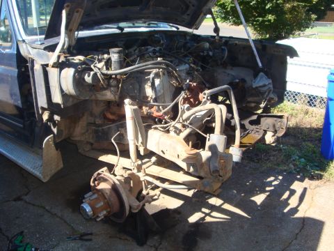 1989 Ford Bronco - The front end of a truck is disassembled, showing the engine and suspension components with the hood open.