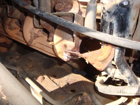 1989 Ford Bronco - Close-up of a rusted bracket supporting an exhaust pipe, with surrounding engine parts.