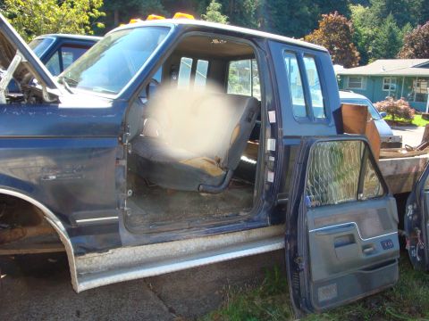 1989 Ford Bronco - Side view of a blue pickup truck cab, showing its interior and flatbed, with the hood open.