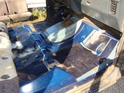 1989 Ford Bronco - Stripped truck cab interior with the seats and carpet removed, exposing a blue-painted floor pan, transmission tunnel with shifter boot ope…