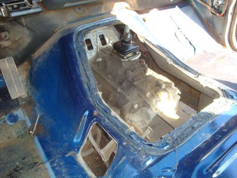 1989 Ford Bronco - Stripped interior of a blue truck with the carpet and console removed, looking down through the open transmission tunnel at a manual gearbo…