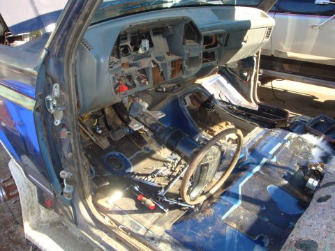 1989 Ford Bronco - Gutted interior of a blue truck shot through the open driver's door, with seats, carpet and center console removed to expose the bare blue-…