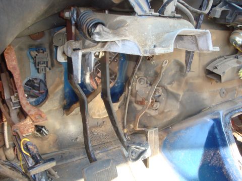 1989 Ford Bronco - Interior of a stripped truck cab with the dash and carpet removed, showing the bare firewall, brake and accelerator pedal assembly, steerin…
