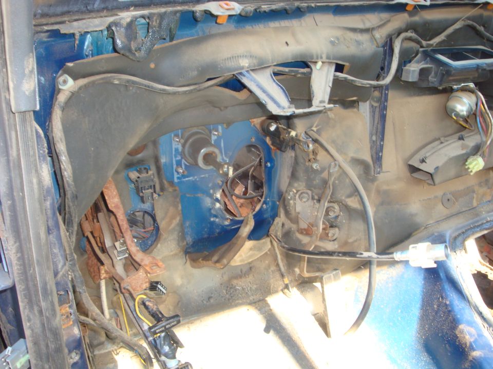Gutted blue Ford truck interior showing bare firewall, parking brake pedal, wiring and heater box