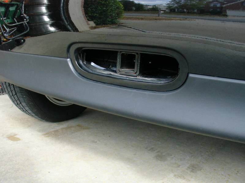 Chrome rectangular exhaust tip in black oval bezel on gray lower bumper of a black car