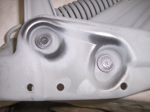 1970 Chevrolet Camaro - Extreme close-up of a freshly primered grey stamped-steel body bracket or hood hinge area, showing two dimpled bolt bosses with factory-mar…
