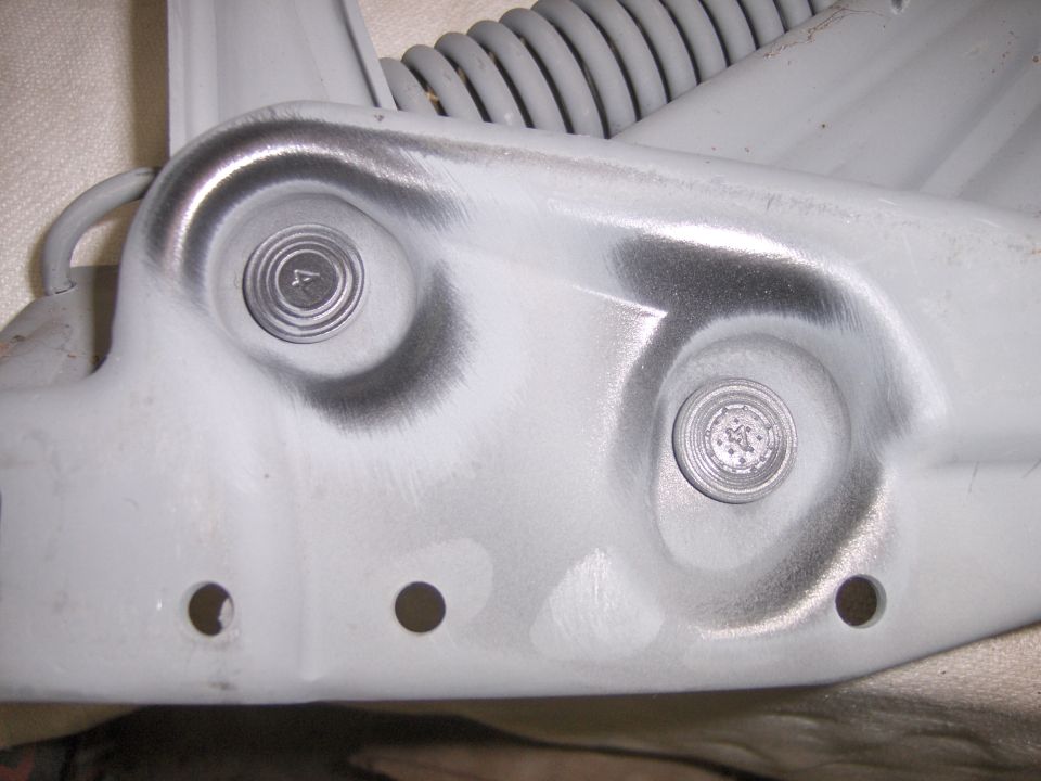 Close-up of grey primered steel bracket with two bolts, coil spring and mounting holes
