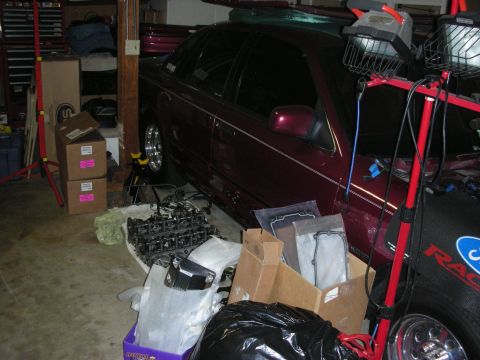 1992 Ford Crown Victoria - Engine parts are laid out on the garage floor next to a dark red 1992 Ford Crown Victoria.