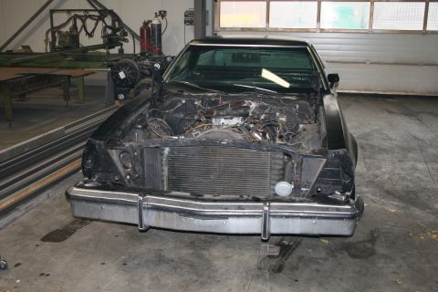 1973 Ford Ranchero - Front view of a black car with its engine compartment open, revealing disassembled parts and exposed mechanics.