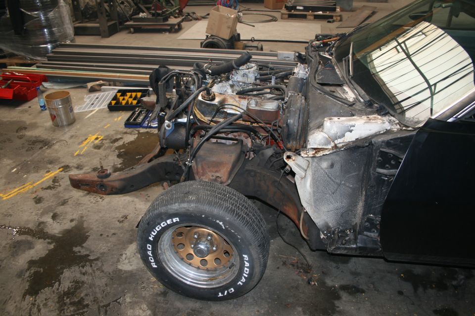 Front end of a black car with engine exposed, in a workshop