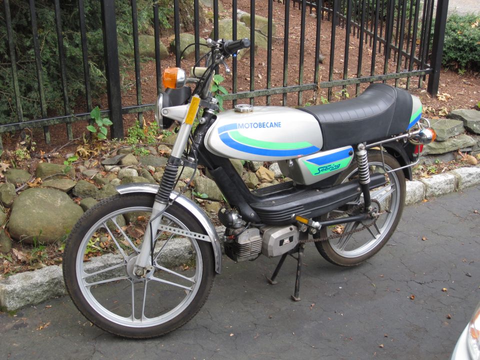 Silver Motobecane Sebring moped with blue and green stripes parked by an iron fence
