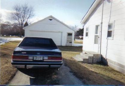 1990 Mercury Grand Marquis - Rear view of a dark blue 1990 Mercury Grand Marquis parked in a driveway next to a white house and garage.