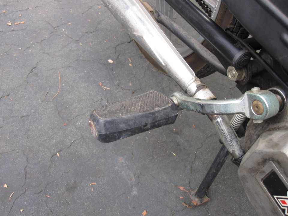 Motorcycle left footpeg, side stand and chrome muffler photographed over cracked asphalt