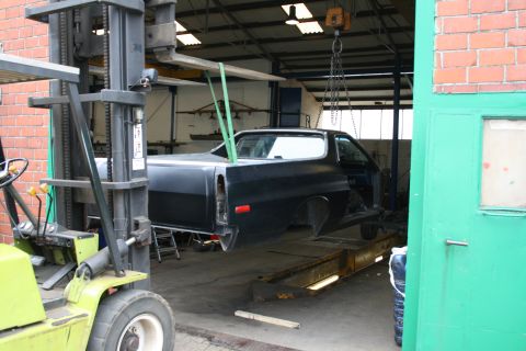 1973 Ford Ranchero - A black 1973 Ford Ranchero is suspended by a hoist and forklift in a workshop, indicating it is undergoing repairs.