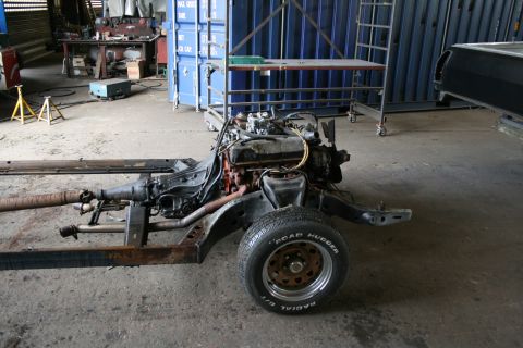1973 Ford Ranchero - The chassis and engine of a vehicle are visible in a workshop setting, with tools and containers in the background.
