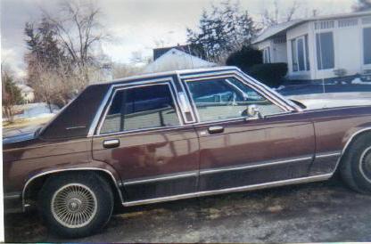 1990 Mercury Grand Marquis - A brown sedan is parked in front of a house on a cloudy day.