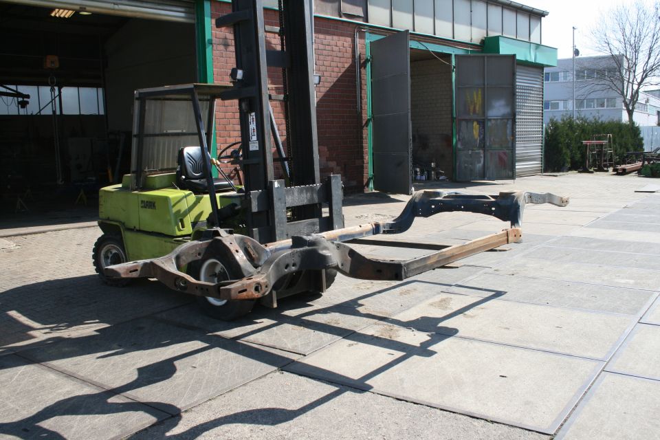 Vehicle frame on a forklift, outdoors, with a garage in the background
