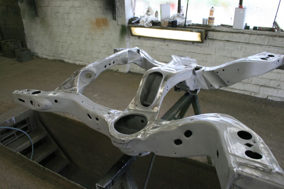 Bare metal car frame assembly on a stand in a workshop