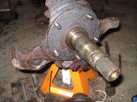 1979 Ford Bronco - Close-up of a heavily rusted vehicle spindle assembly, supported by orange jack stands in a garage.