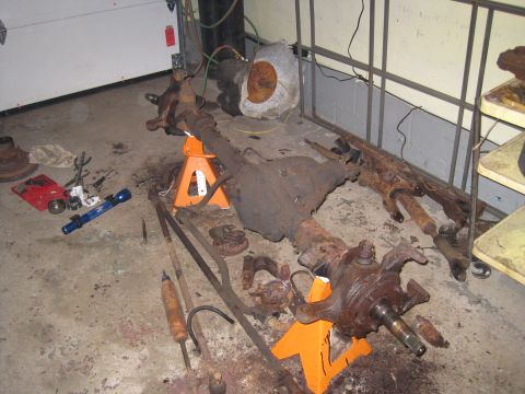 1979 Ford Bronco - Disassembled front axle assembly and associated parts are laid out on a garage floor.