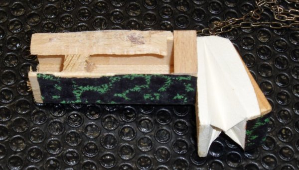 Wooden block with green patterned fabric and white paper attached, resting on a black bubble-wrap surface